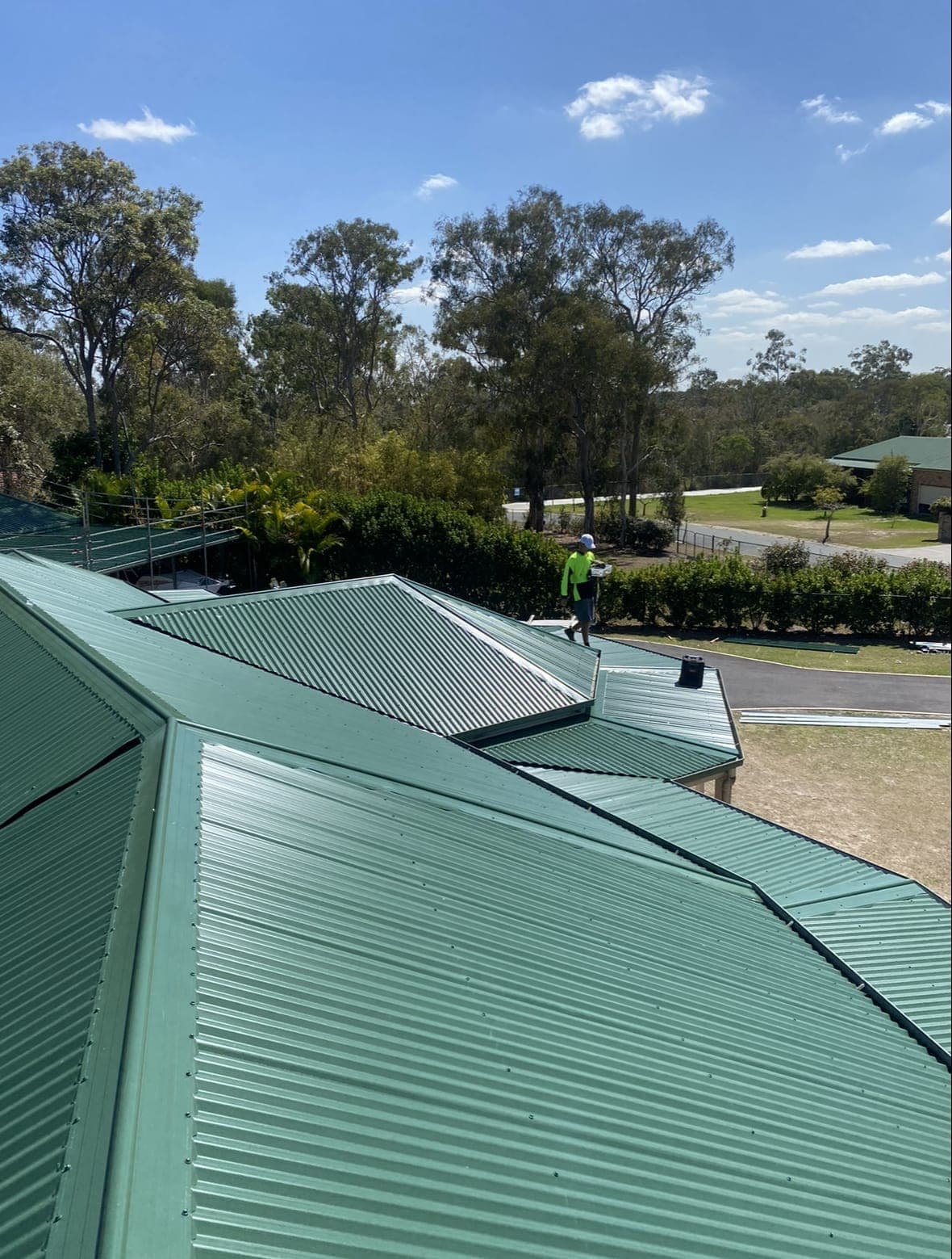 Top Tin roofer working on a new green Colorbond roof on a large family home